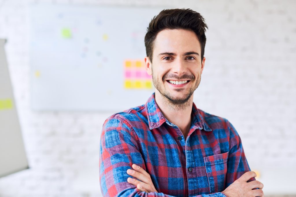 Portrait of young handsome man looking at camera while standing in alternative modern office
