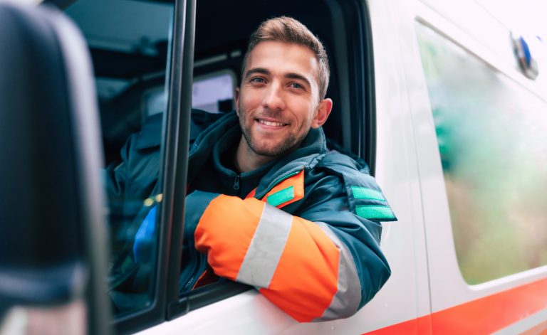Professional and confident young paramedic looking on the camera with ambulance background