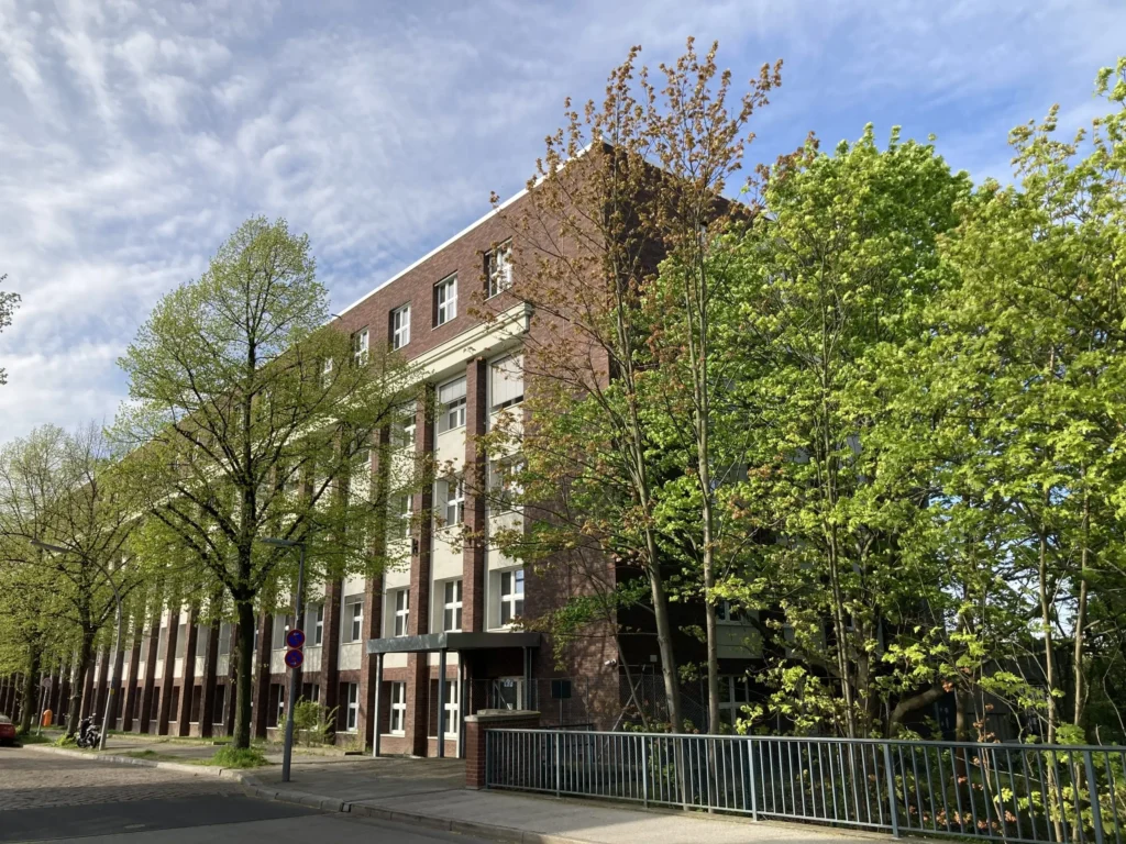 Außenansicht des Gebäudes der Akkon Hochschule für Humanwissenschaften mit umliegenden Bäumen.