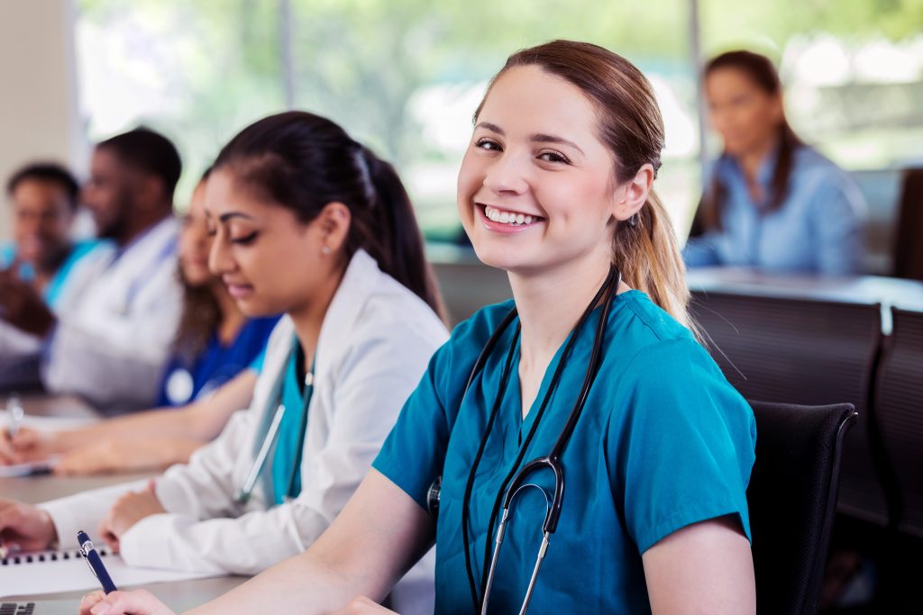 Cheerful young female nursing school student smiles during class. She is looking at the camera.