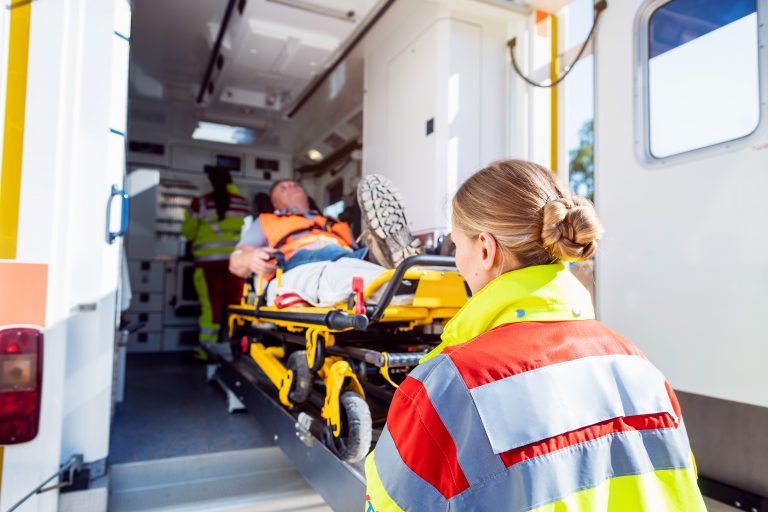 Paramedics in uniform putting injured man on stretcher in ambulance car