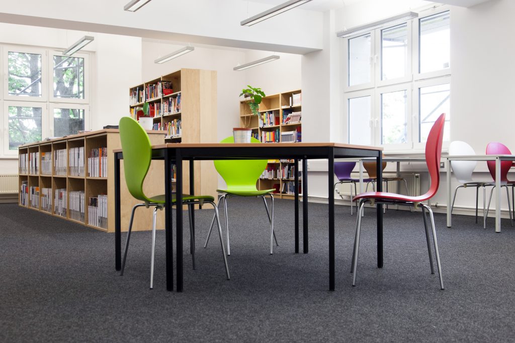 Heller Bibliotheksraum mit Arbeits­tischen, bunten Stühlen und Bücherregalen.