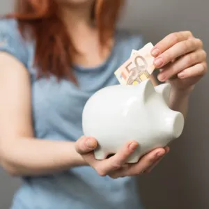 close-up of person putting a 50 euro bill in a piggy bank
