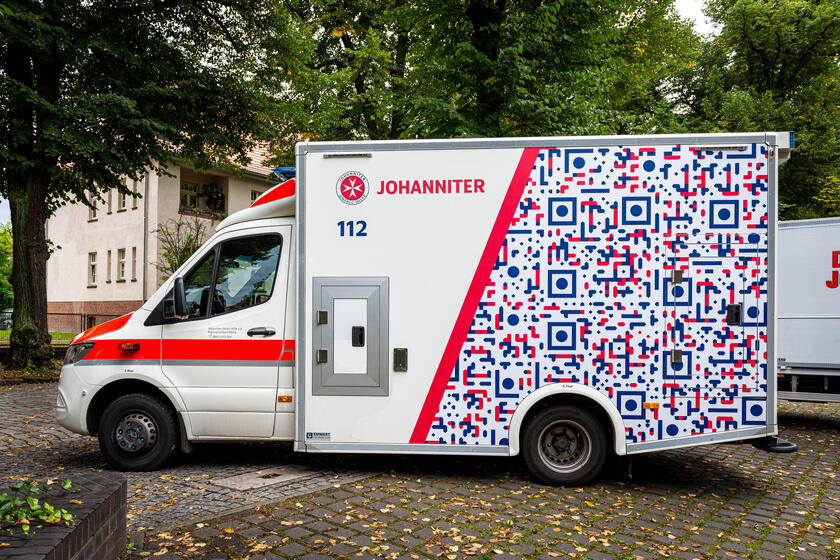 Ein Einsatzfahrzeug mit auffälliger, bunt gestalteter Seitenbeklebung steht im Freien auf einem Parkplatz. Das Fahrzeug trägt das Logo der Johanniter und ist als mobiles Angebot gekennzeichnet.