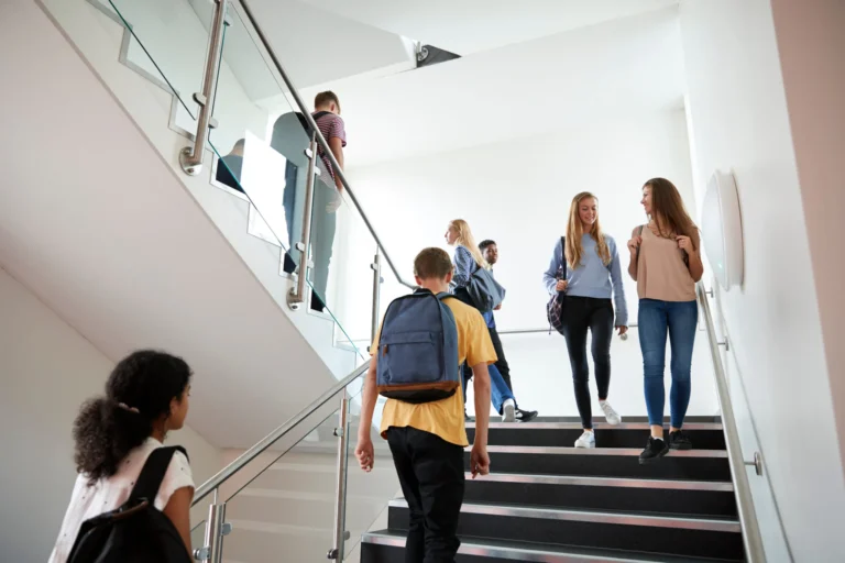 Studierende mit Rucksäcken gehen gemeinsam eine Treppe in einem modernen Hochschulgebäude hinauf.