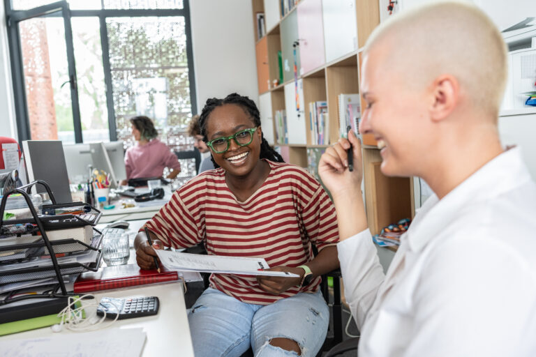 Zwei Personen im Gespräch an einem Arbeitsplatz in einem offenen Büro.