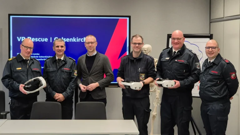 Vertreter der Feuerwehr präsentieren bei einer Veranstaltung auf einer Bühne Ausrüstungsgegenstände und stehen gemeinsam vor einem Veranstaltungsbanner.