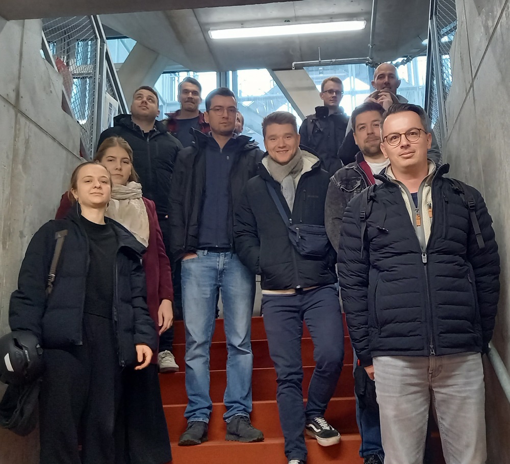 Gruppe von Studierenden und Begleitpersonen auf einer Treppe mit rotem Teppich im Innenbereich eines Gebäudes.