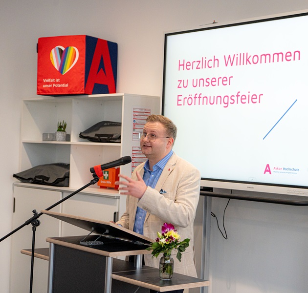 Redner am Podium vor Präsentationsfolie zur Standorteröffnung der Akkon Hochschule.