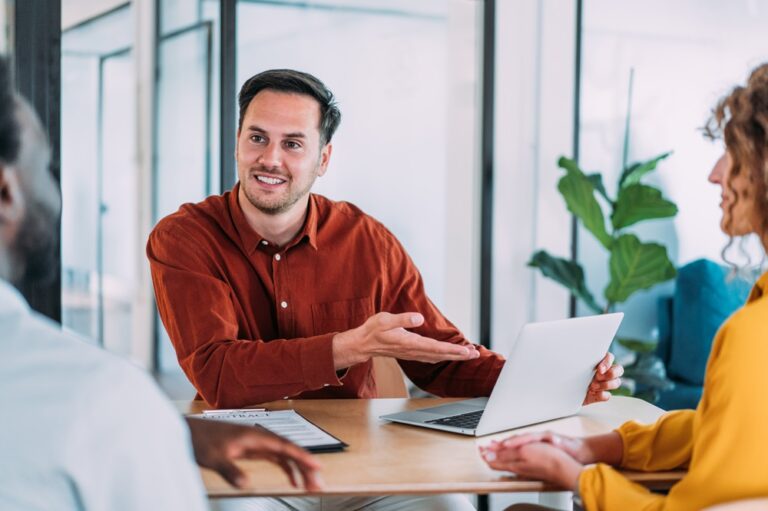 Mann sitzt an einem Tisch und arbeitet mit Laptop und Tablet in einem modernen Büro.