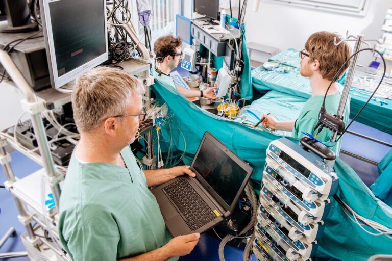 Mehrere medizinische Fachkräfte arbeiten in einem OP-ähnlichen Umfeld mit Monitoren, Geräten und Laptop und bereiten einen Eingriff vor.