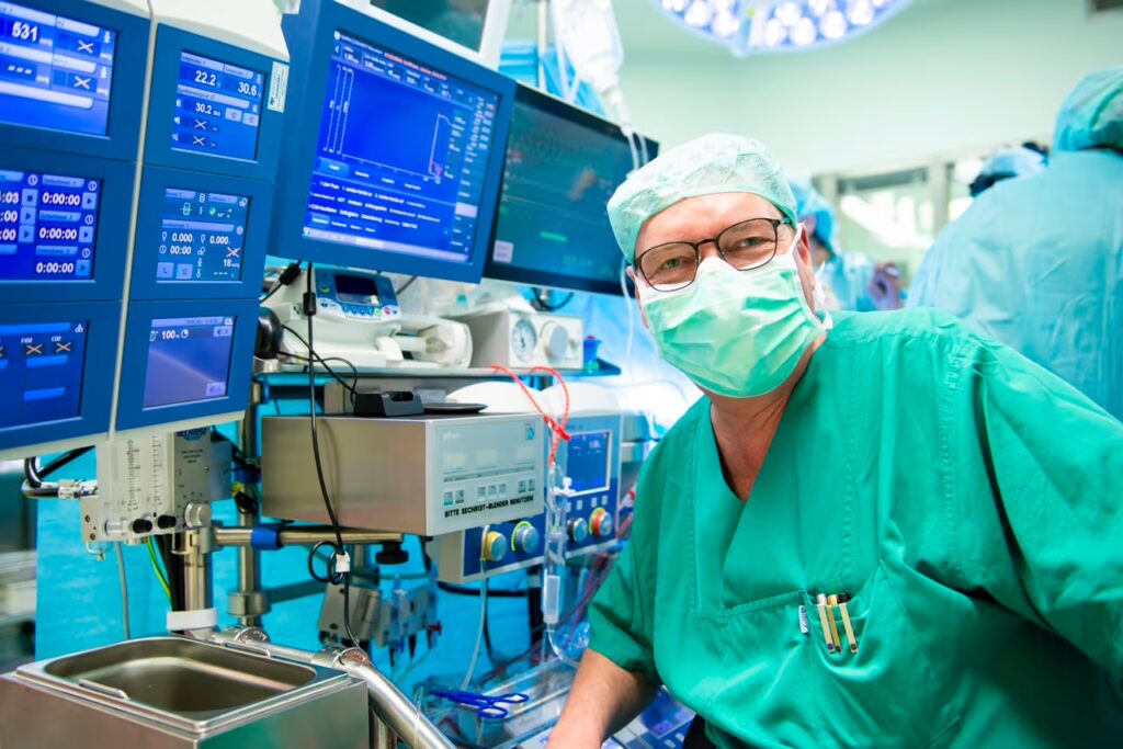 Medizinischer Facharzt in OP-Kleidung und Schutzmaske arbeitet in einem Operationssaal neben Monitoren und medizinischen Geräten.