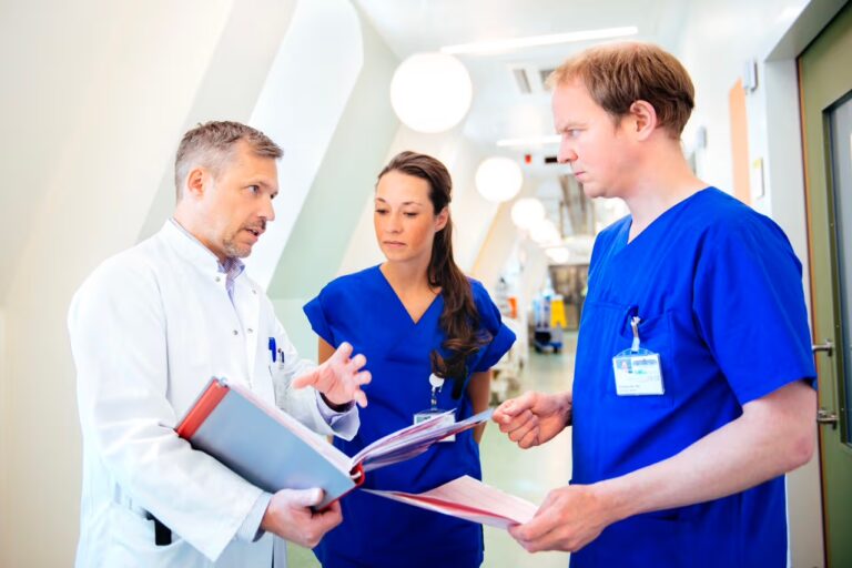 Drei medizinische Fachkräfte besprechen sich auf einem Klinikflur und schauen gemeinsam in Unterlagen.