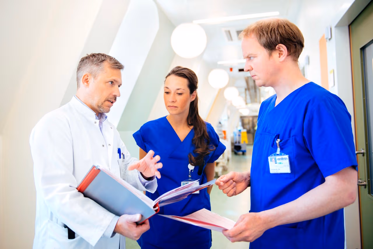 Drei medizinische Fachkräfte besprechen sich auf einem Klinikflur und schauen gemeinsam in Unterlagen.