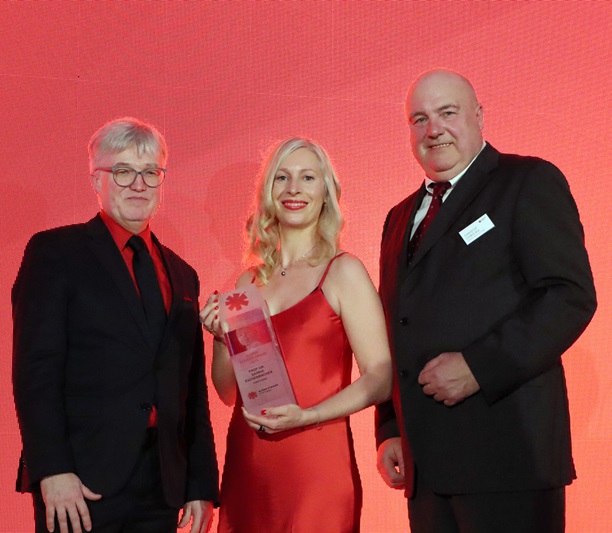 Preisträgerin erhält einen Björn Steiger Award auf einer Bühne und hält die Auszeichnung in den Händen, flankiert von zwei Männern bei der Preisverleihung.