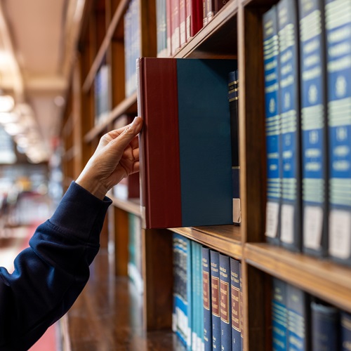 Hand greift in ein Bücherregal mit Fachbüchern in einer Bibliothek