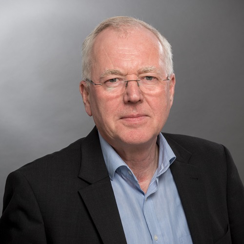 Porträt eines Mannes mit Brille in dunklem Sakko vor grauem Hintergrund