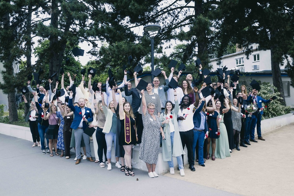 Absolvent*innen, Angehörige sowie Mitarbeitende der Akkon Hochschule versammeln sich nach der Abschlussfeier für ein gemeinsames Gruppenfoto im Außenbereich. Die Teilnehmenden blicken in die Kamera und feiern gemeinsam den erfolgreichen Studienabschluss.