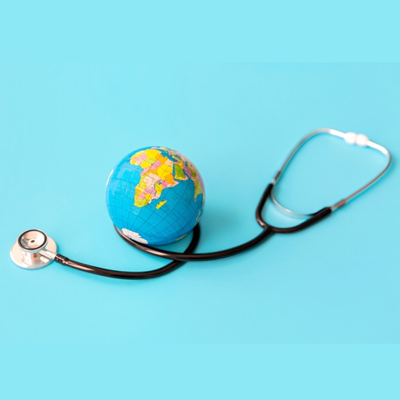 Ein Globus liegt auf einem hellblauen Hintergrund und ist von einem Stethoskop umgeben. Das Motiv symbolisiert die Verbindung von Gesundheit, Medizin und globalen Herausforderungen im internationalen Kontext.