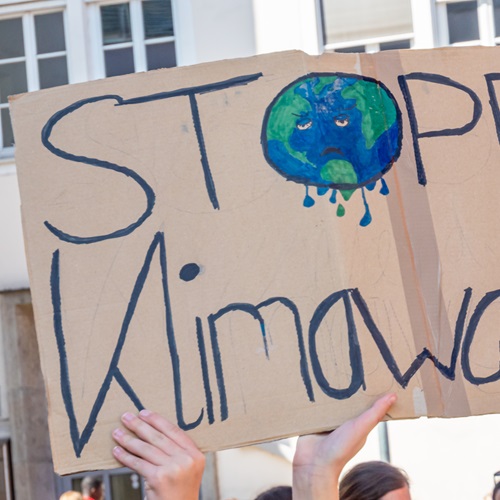 Eine Person hält ein handgemaltes Protestplakat mit der Aufschrift „STOP Climate“. Das Wort „Climate“ ist teilweise durch eine Illustration der Erde ergänzt. Das Schild steht symbolisch für Engagement im Klima- und Umweltschutz.