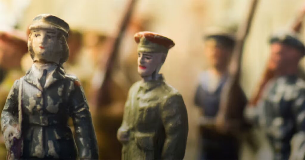 Unscharfe Darstellung mehrerer historischer Militärfiguren in Uniform. Im Vordergrund stehen zwei Soldatenfiguren, während weitere Figuren im Hintergrund zu erkennen sind. Die Aufnahme wirkt wie eine Nahaufnahme von Miniaturen oder Modellfiguren und ist in warmen Farbtönen gehalten.