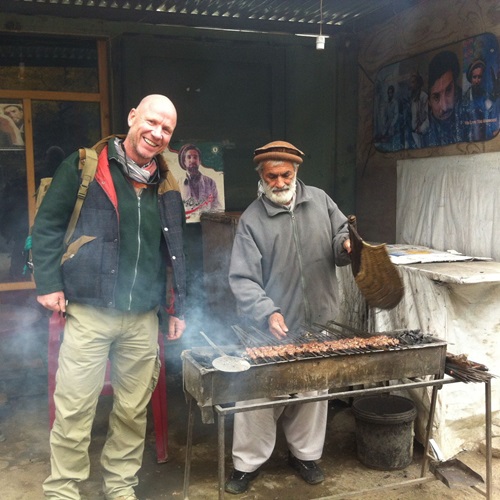 Karl Rüdiger Tillmann steht gemeinsam mit einem Mann an einem Grill und bereitet Essen in einer einfachen Außenküche während eines internationalen Einsatzes zu.