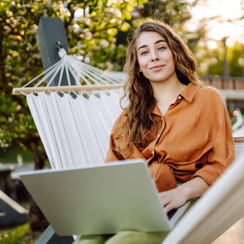 Studentin lernt mit einem Laptop in einer Hängematte im Freien – flexibles und ortsunabhängiges Online-Studium.