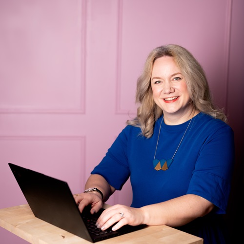 Porträt von Dr. Anke Jentzsch an einem Schreibtisch mit Laptop vor einem rosa Hintergrund.