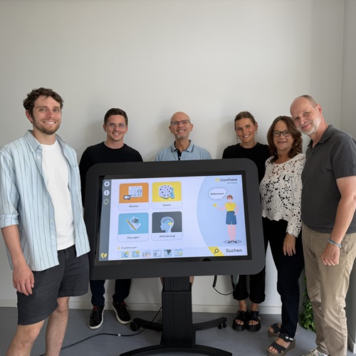 Vier Personen stehen gemeinsam um einen digitalen Aktivitätstisch mit Touchscreen.