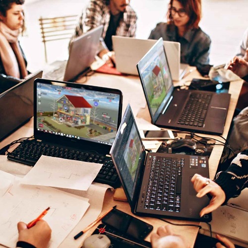Studierende arbeiten gemeinsam mit Laptops und Tablets an einem Tisch.