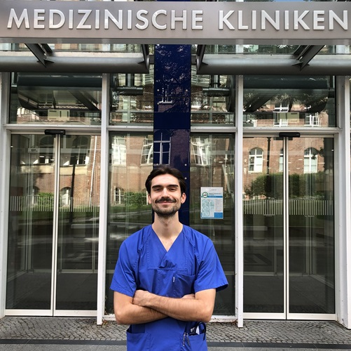 Mann in blauer medizinischer Kleidung vor dem Eingang einer Klinik.