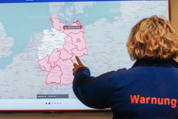 Person vor einer Deutschlandkarte mit farblich markierten Warngebieten und eingeblendeter Warnmeldung.