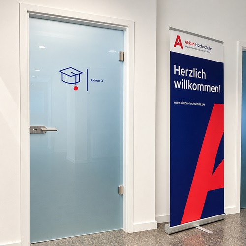 Eingangsbereich der Akkon Hochschule mit Glastür und Akkon-Aufsteller.