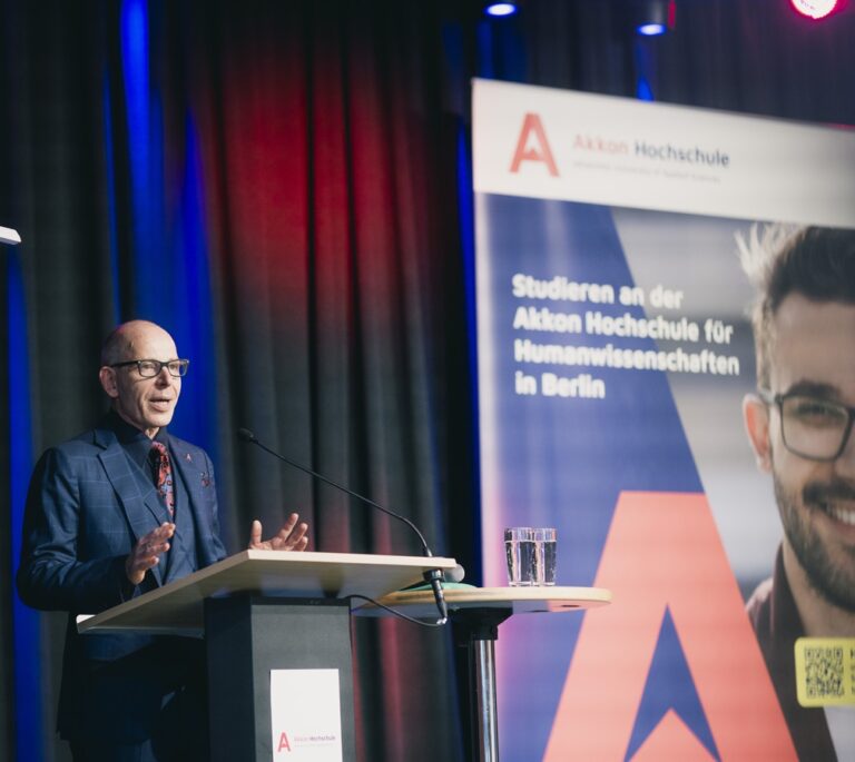 Prof. Dr. Andreas M. Bock, Präsident der Akkon Hochschule, spricht bei der Immatrikulationsfeier am Rednerpult. Im Hintergrund ist ein Banner der Akkon Hochschule zu sehen.